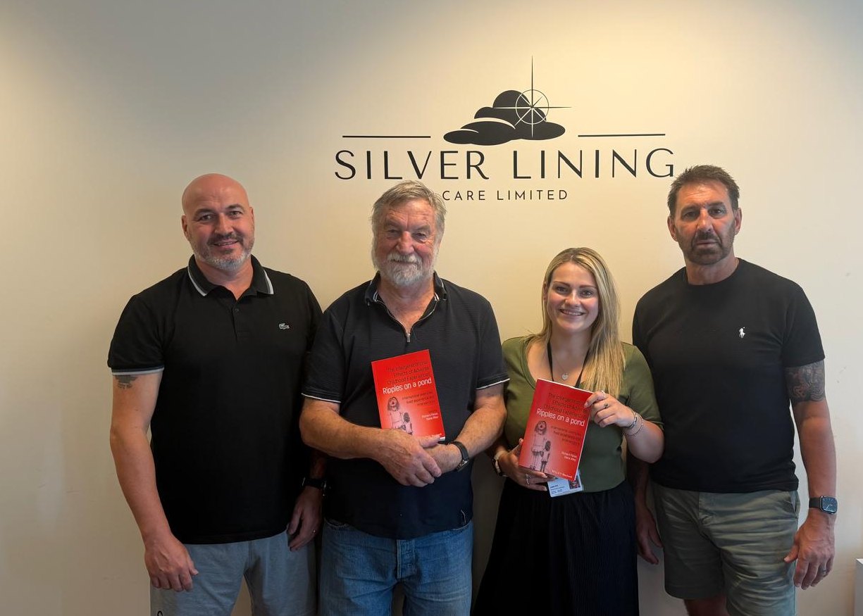Dr Richard Pates and members of our leadership team in front of the Silver Lining Care sign at our Head Office, two of them holding copies of his new book.